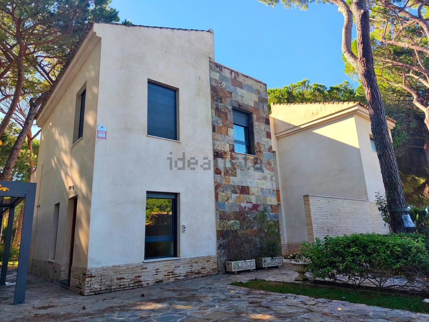 Fachada de la casa de Acebuche, con revestimiento de piedra y pinos.