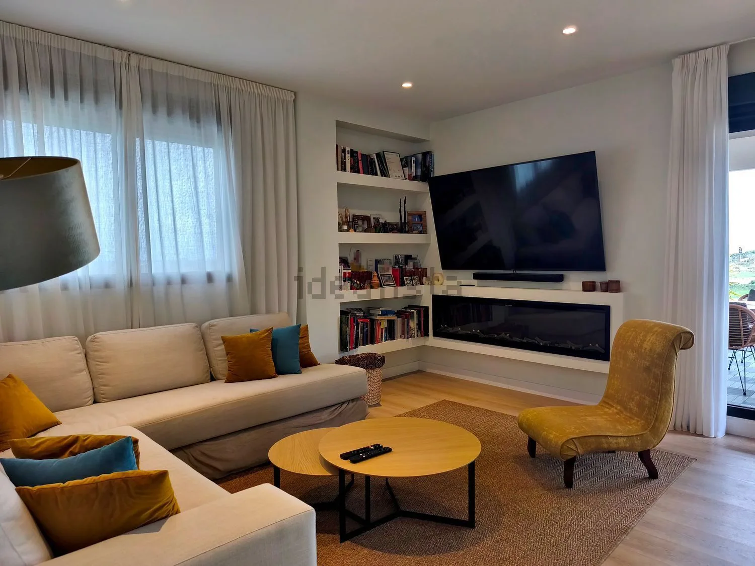 Zona de estar del ático con sofá, estantería y chimenea bajo el televisor.